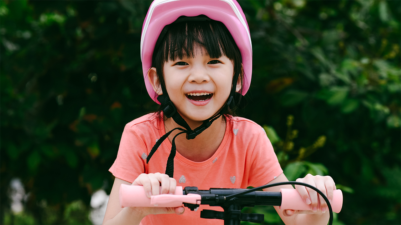 A girl in a pink helmet rides a pink e-scooter. 