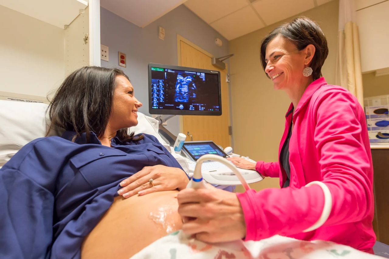 Doctor holds ultrasound wand on pregnant patients belly while seeing baby on the screen and smiling at each other.