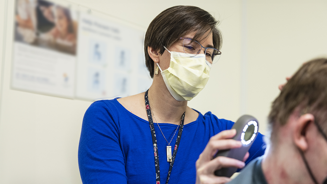 Dr. Anna Bruckner uses light to examine back neck of a patient 