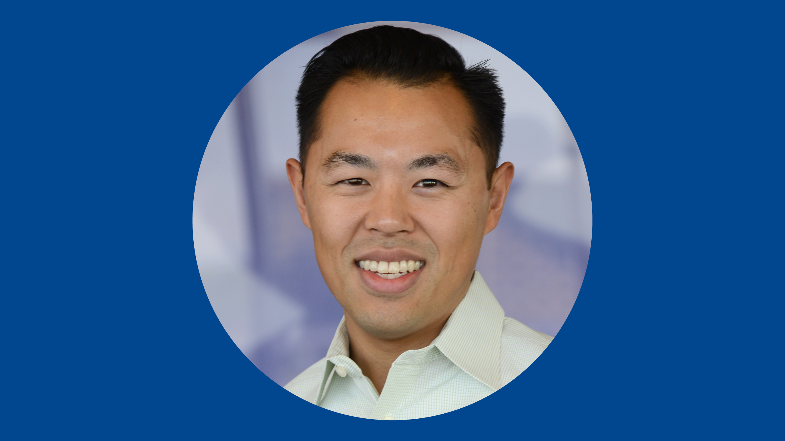 Dr. John Kim wearing a light green shirt and smiling with a blue background. 