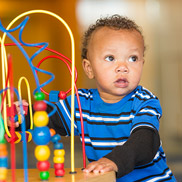 Pediatrics Emergencies A toddler wearing a blue striped shirt plays with a wooden maze toy.