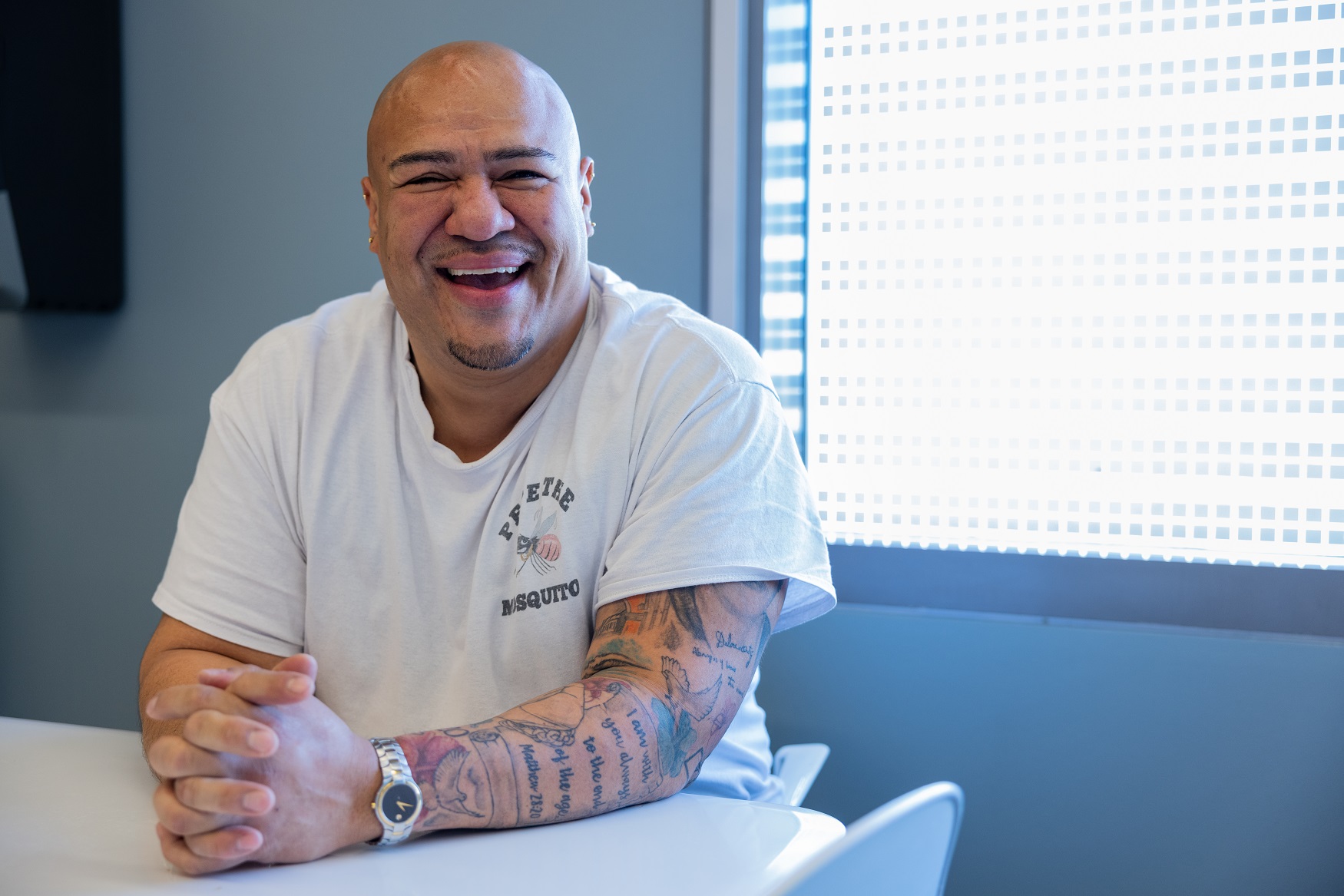 Man sitting at a break room table with his hands clasped on the table smiling. 