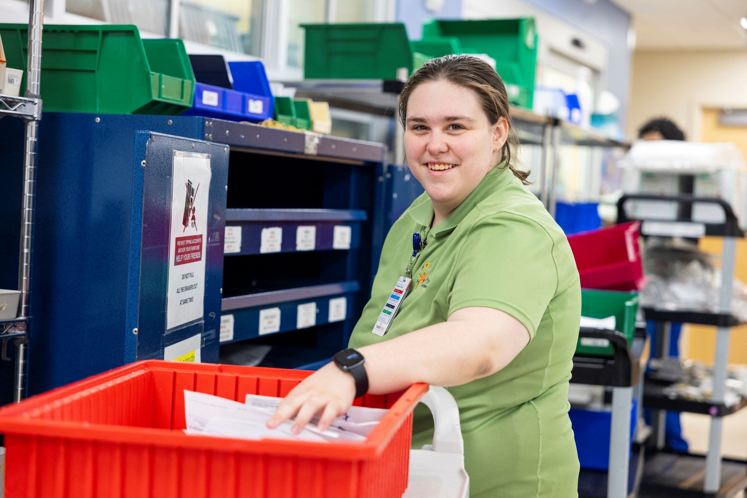 A person wearing a light green shirt smiles as they sort paperwork in a workroom at Children’s Hospital Colorado.