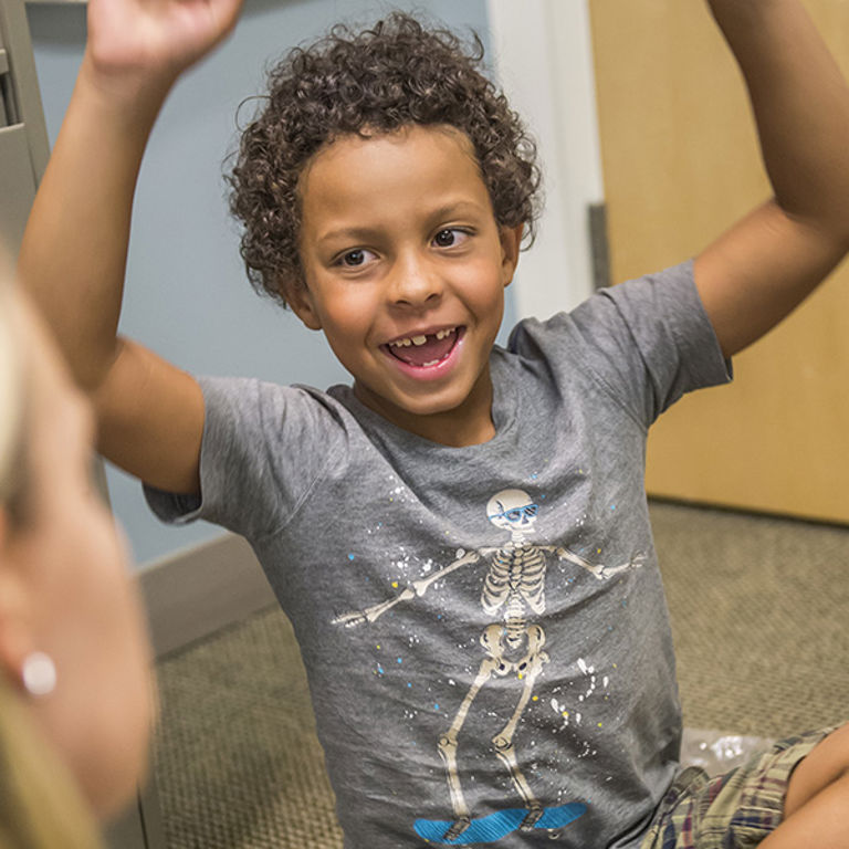 A kid sits on the floor with a doctor, arms raised.