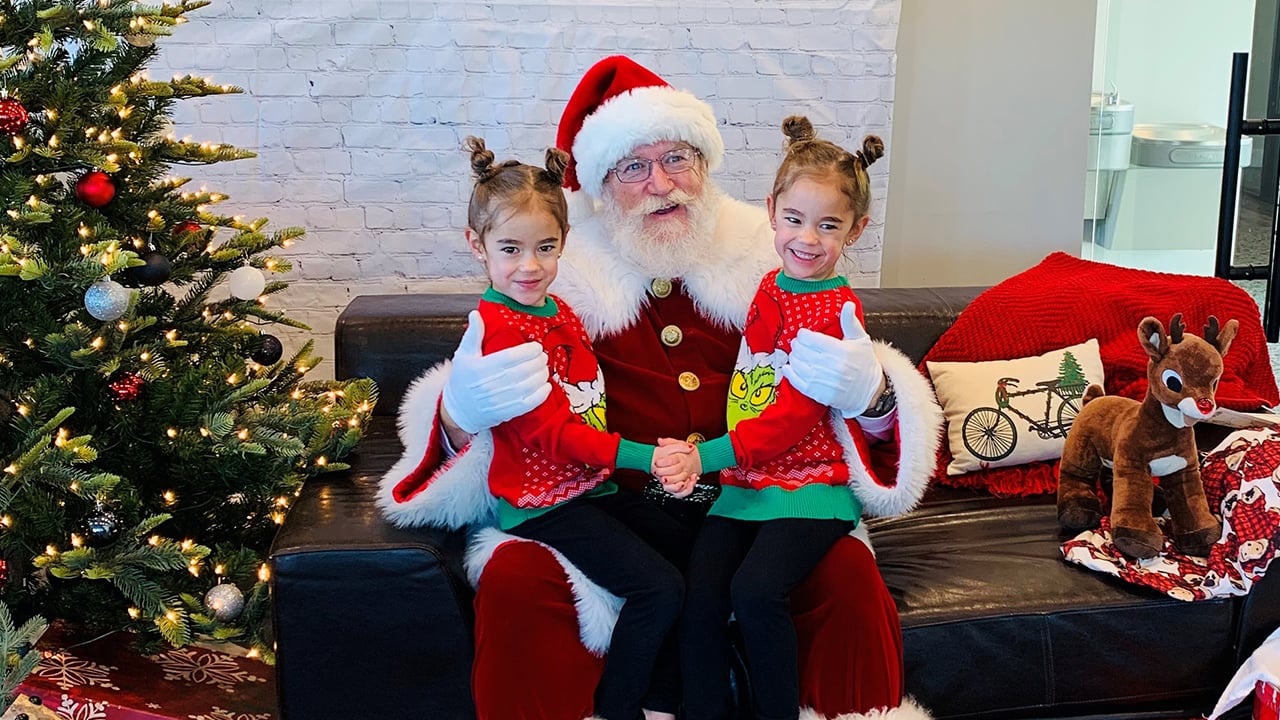 Zoey and Kenna sit on Santa's lap in matching Grinch sweaters