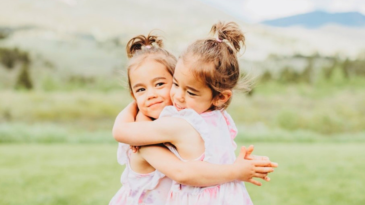 Zoey and Kenna hug tightly in front of a serene outdoor background