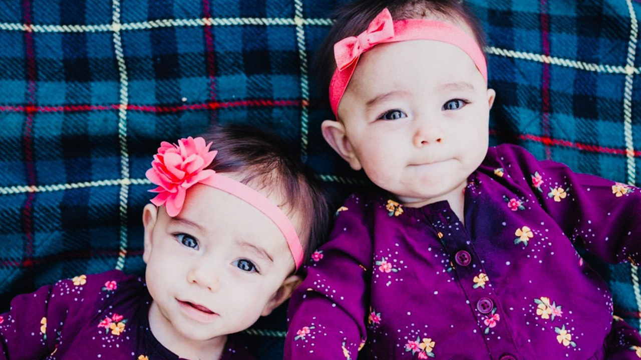 Zoey and Kenna as babies in matching outfits lie on a blanket