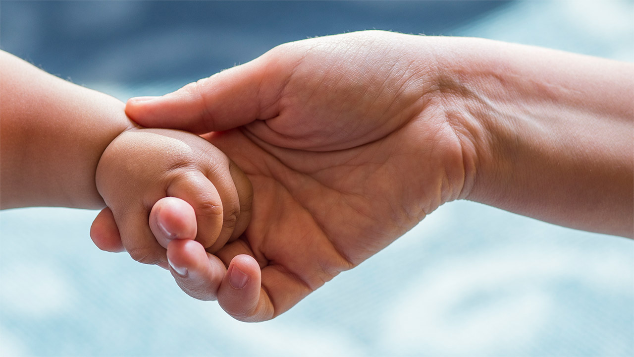 A closeup of a baby's hand grasping a doctor's finger.