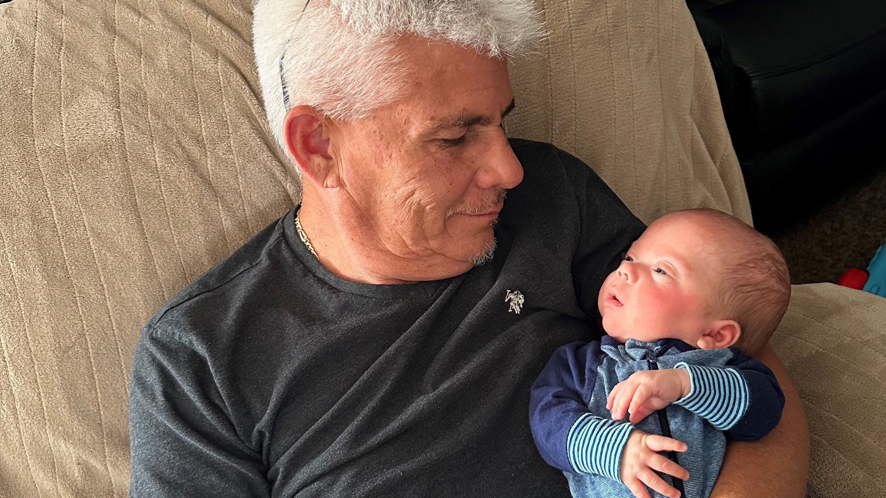 Emilio's grandfather holds the baby as he smiles.