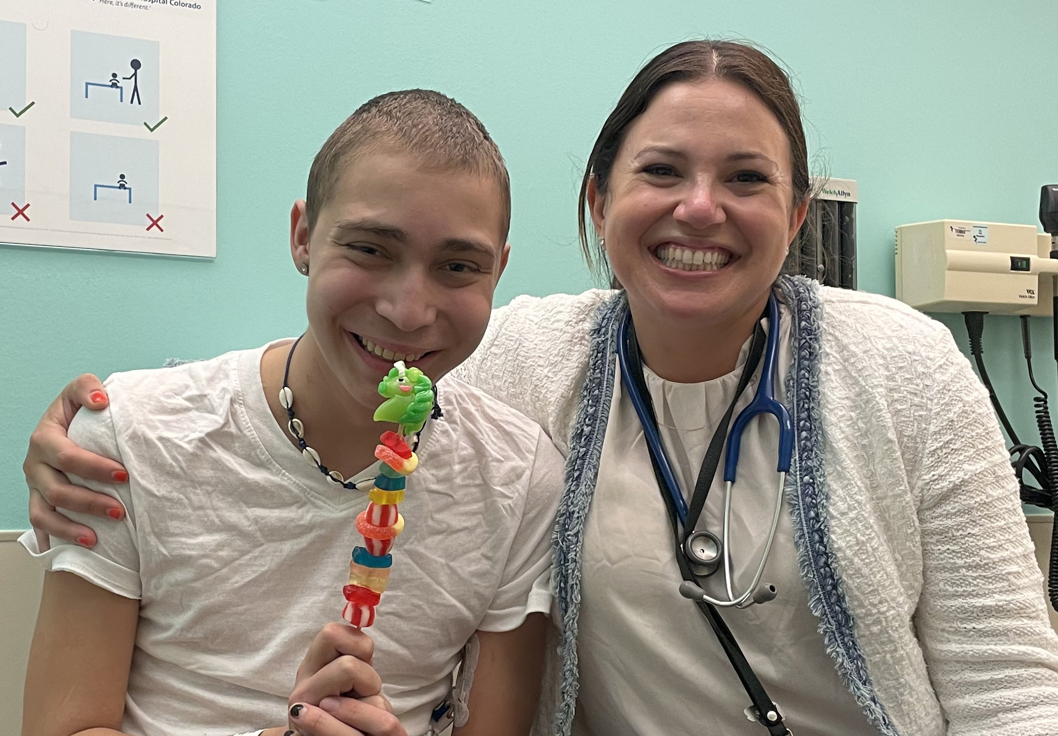 Seth smiles next to a provider in an exam room while he holds up a treat made of candies on a skewer. 