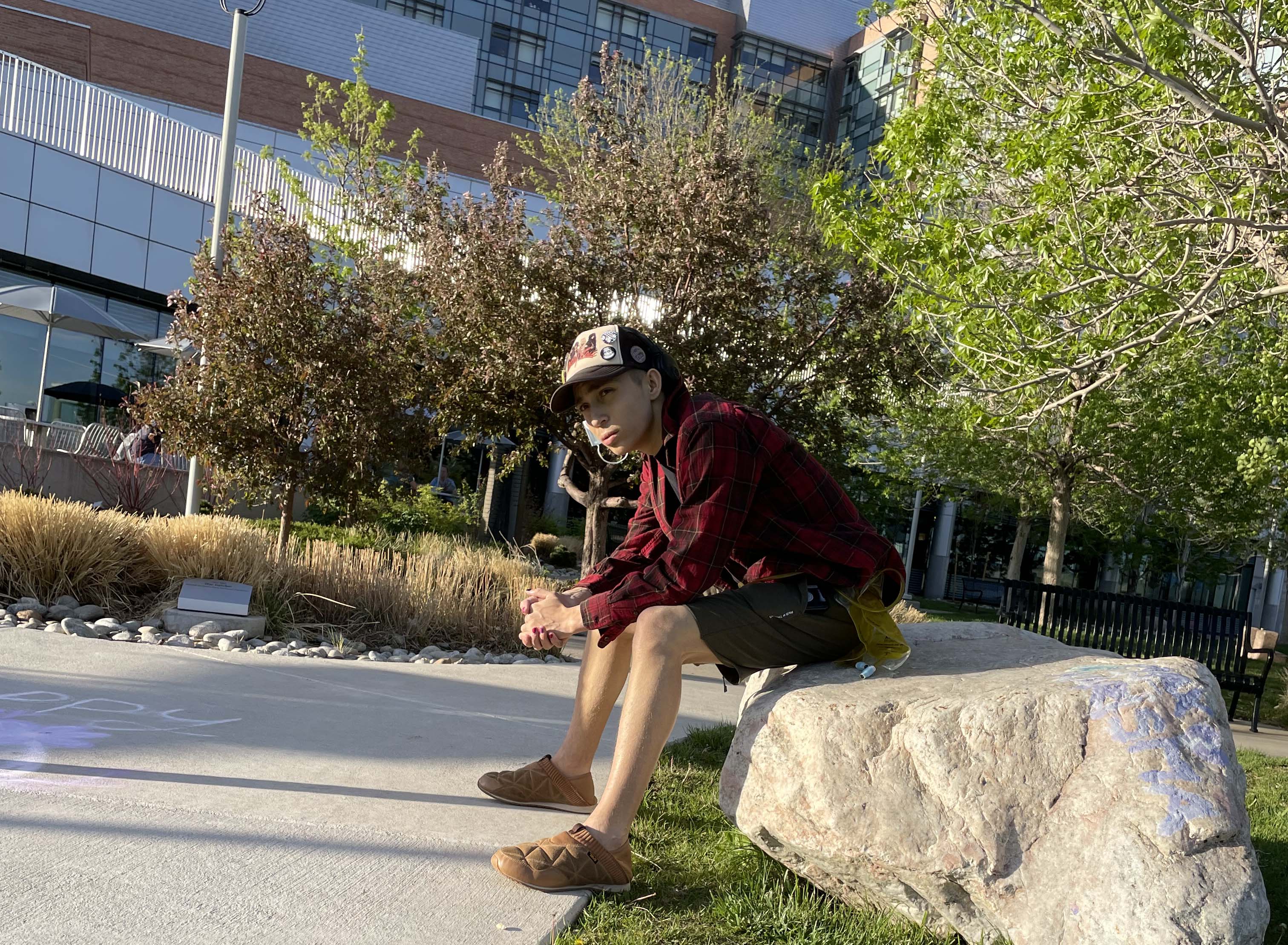 Seth sits outside on one of the large rocks on the Children's Hospital Colorado campus.