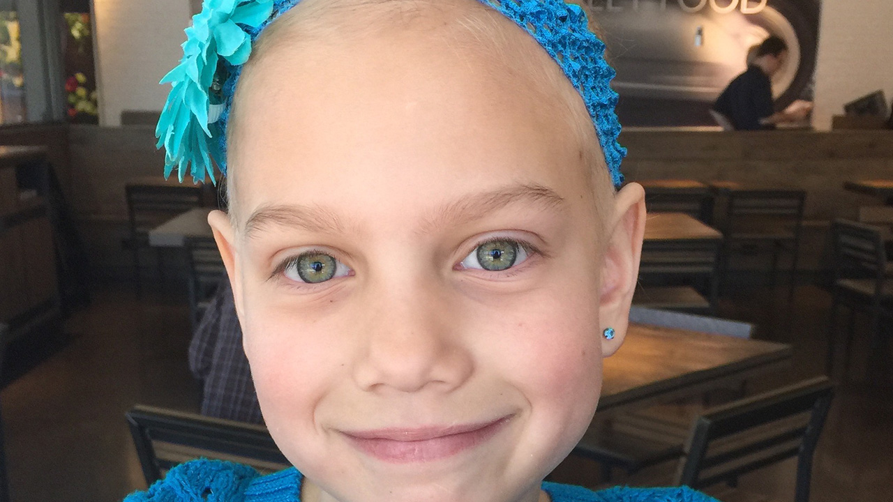 A child wearing a blue headband and sweater, smiling at the camera.