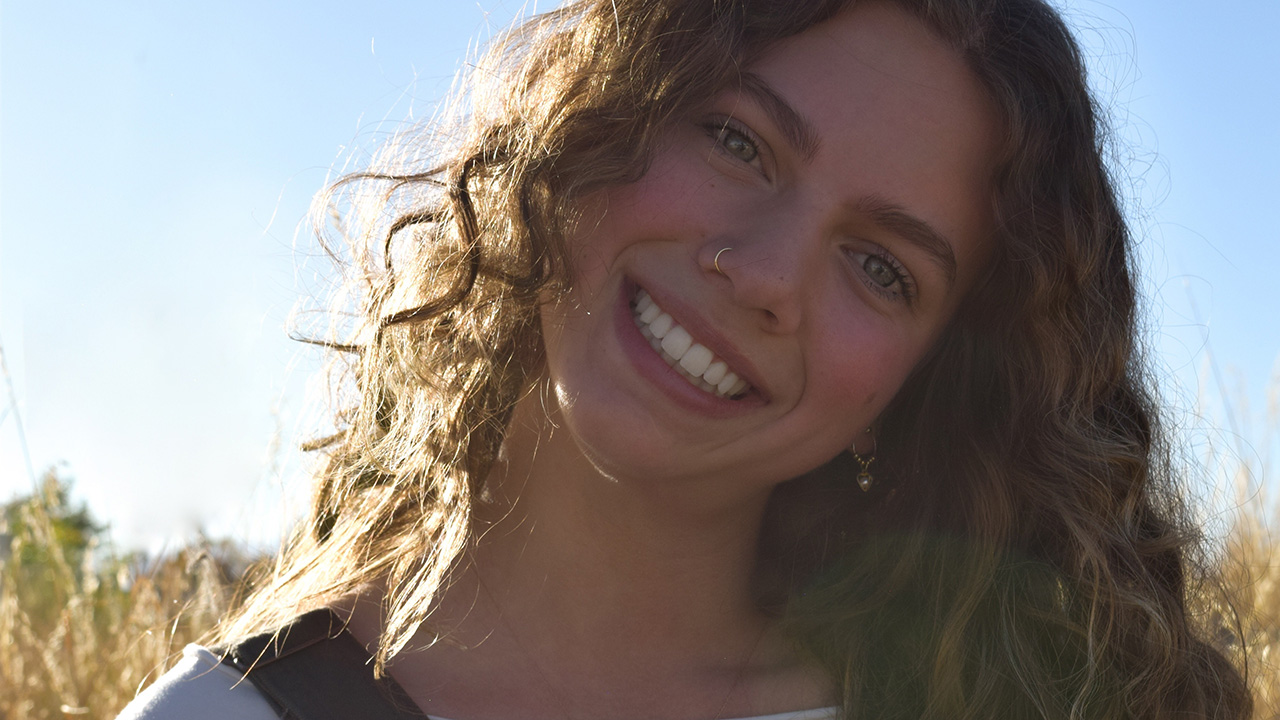 A girl with curly hair smiling in a sunny field.