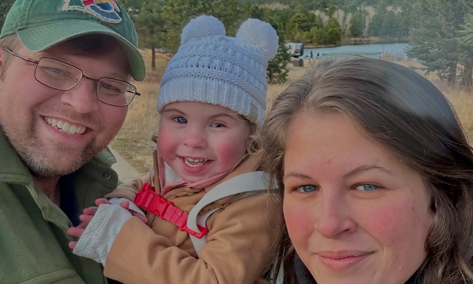 Willow smiling with her parents with a lake and mountains in the background