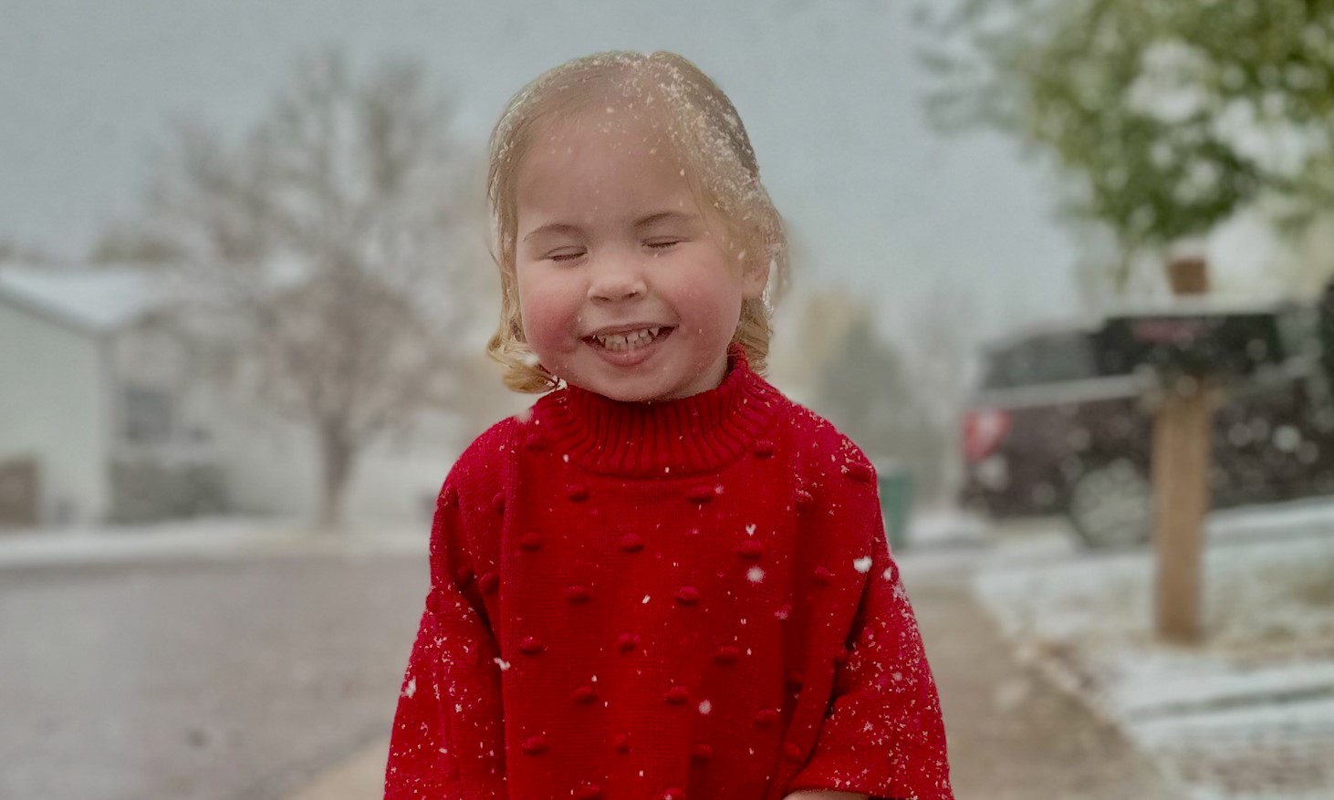 Willow smiling while standing on the sidewalk as snow falls around her