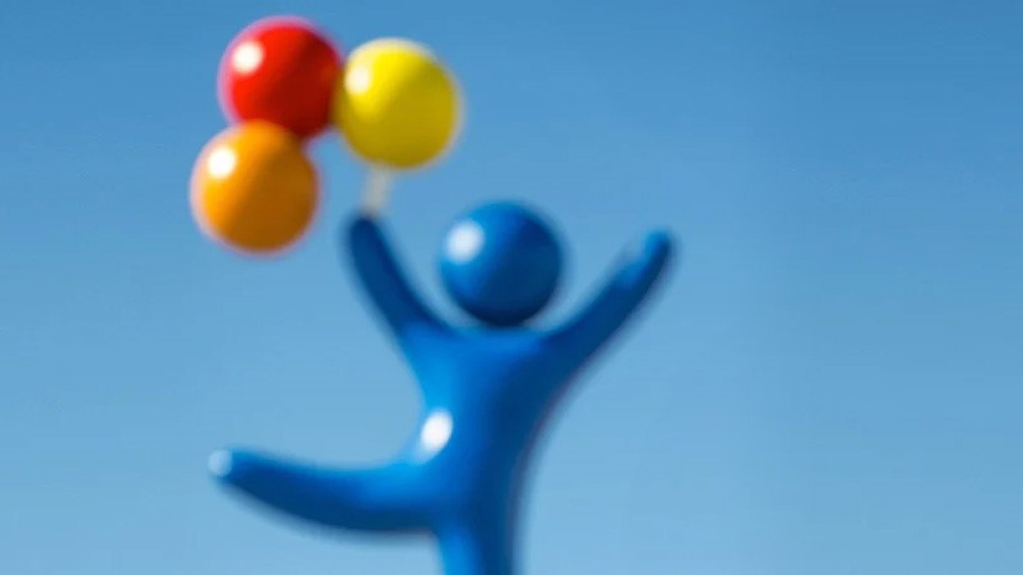 A bright blue background with the "balloon boy" off center to the right. The balloon boy is a blue character who appears to be soaring by holding red, orange and yellow balloons above his head.