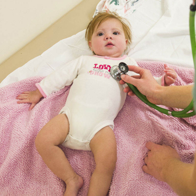 A baby lays on an exam table while a provider uses a stethoscope. 