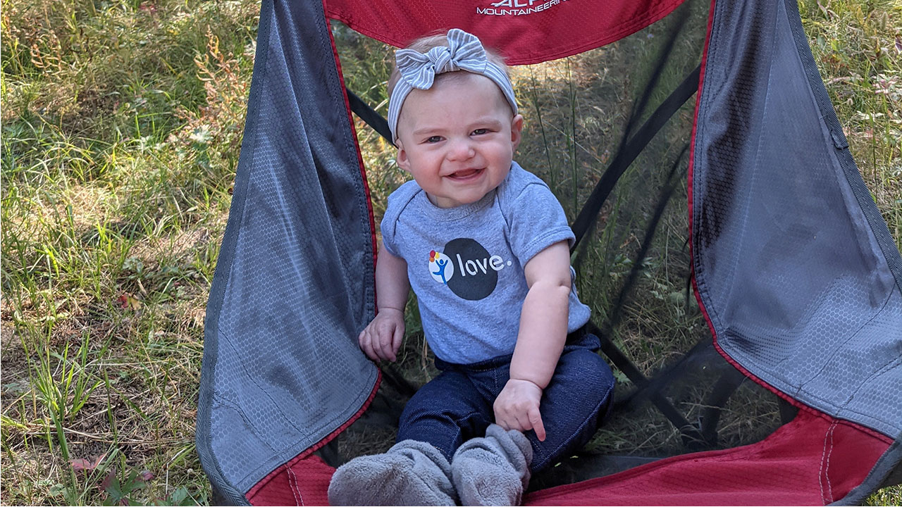 An infant girl sits smiling in a camping chair. She received care for fetal heart block at Children’s Colorado.