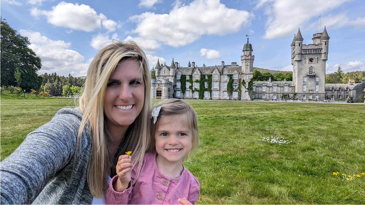 A toddler girl stands with her mom in front of a grass field and a castle in Ireland.