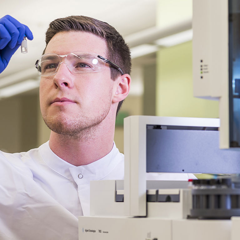 A lab technician holds up a small tube to inspect it