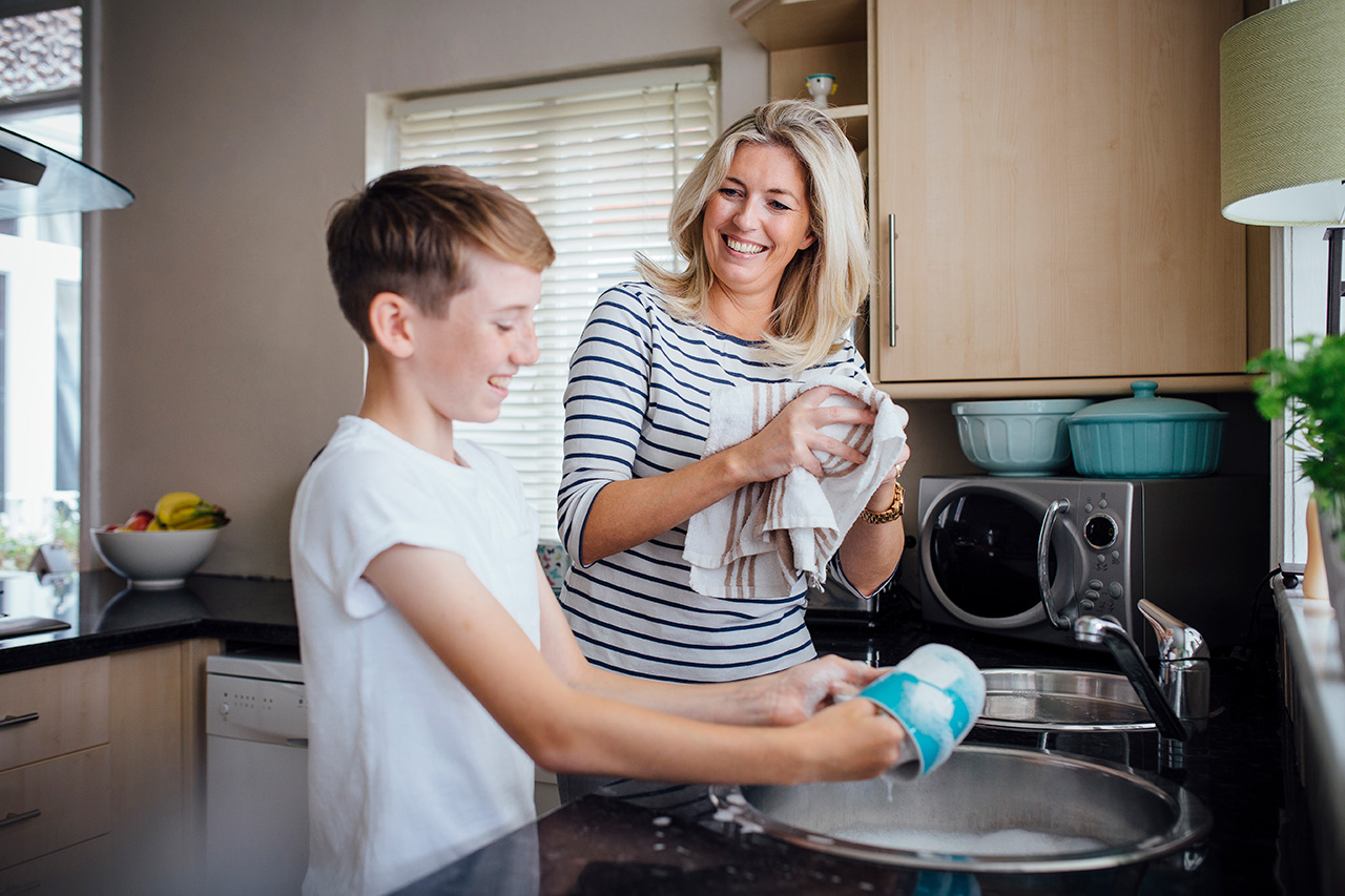 A mother and her pre-teen child wash dishes together.