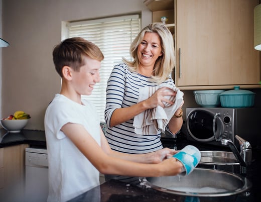 A mother and her pre-teen child wash dishes together.