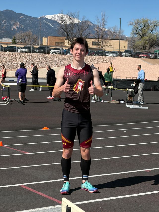 A boy standing on a running track giving a thumbs up