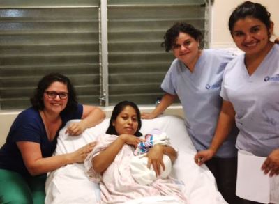 A birth center patient sits in a bed holding her newborn baby.