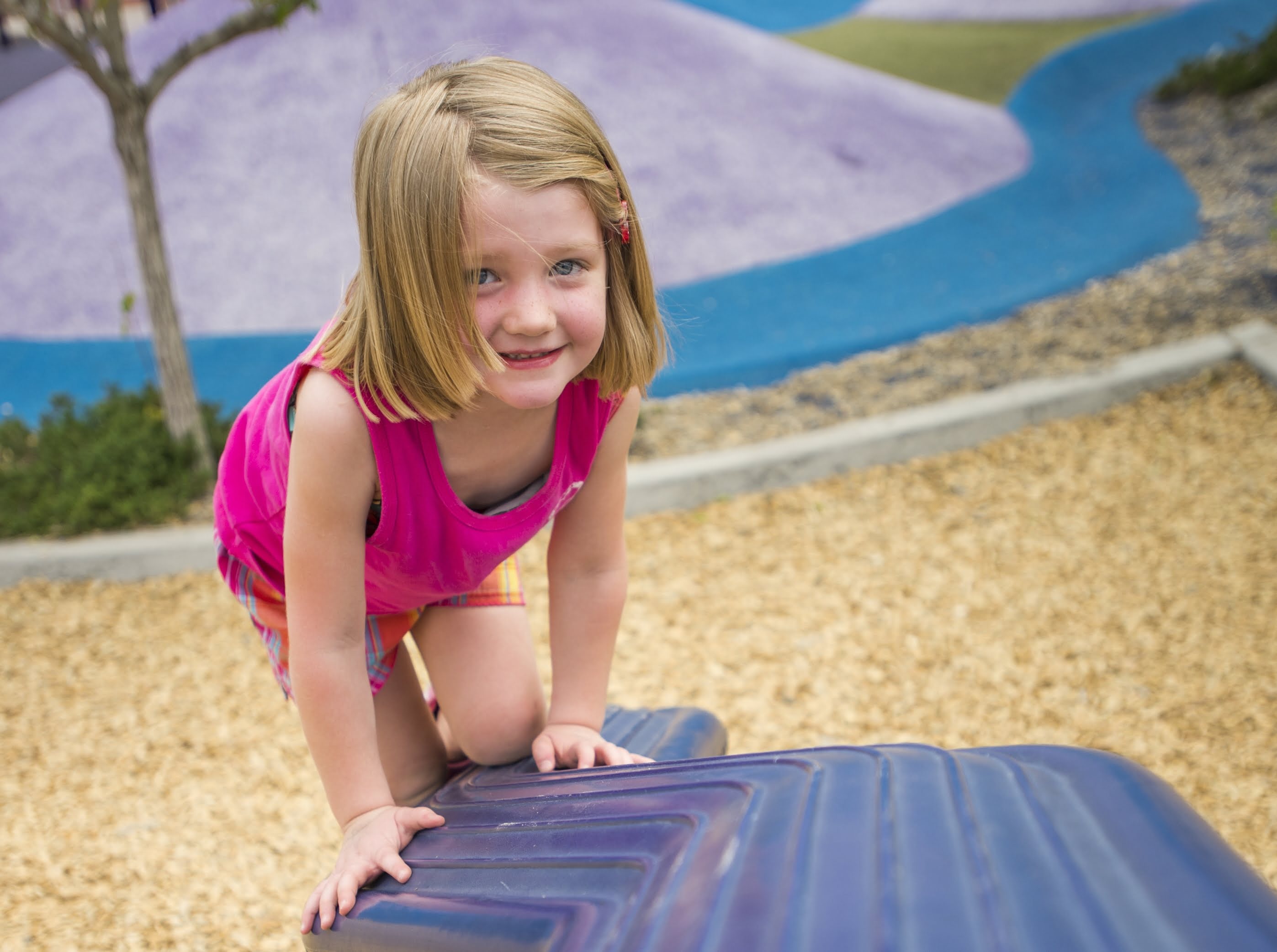 A girl with blonde hair and wearing a pink tank top plays at a playground.