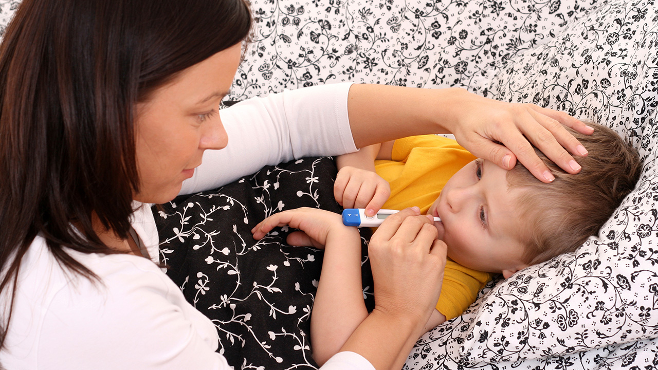 A parent places their hand on the forehead of a sick child while taking their temperature with a thermometer.