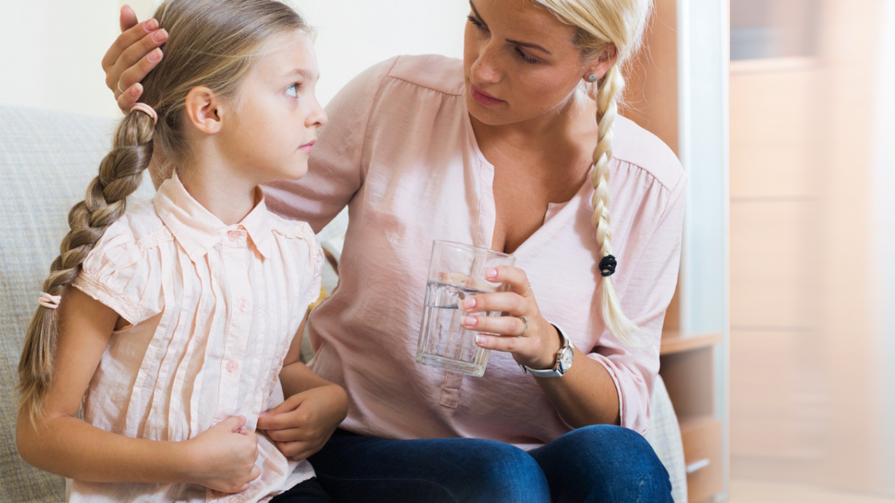 A girl holds her stomach while her mom comforts her.