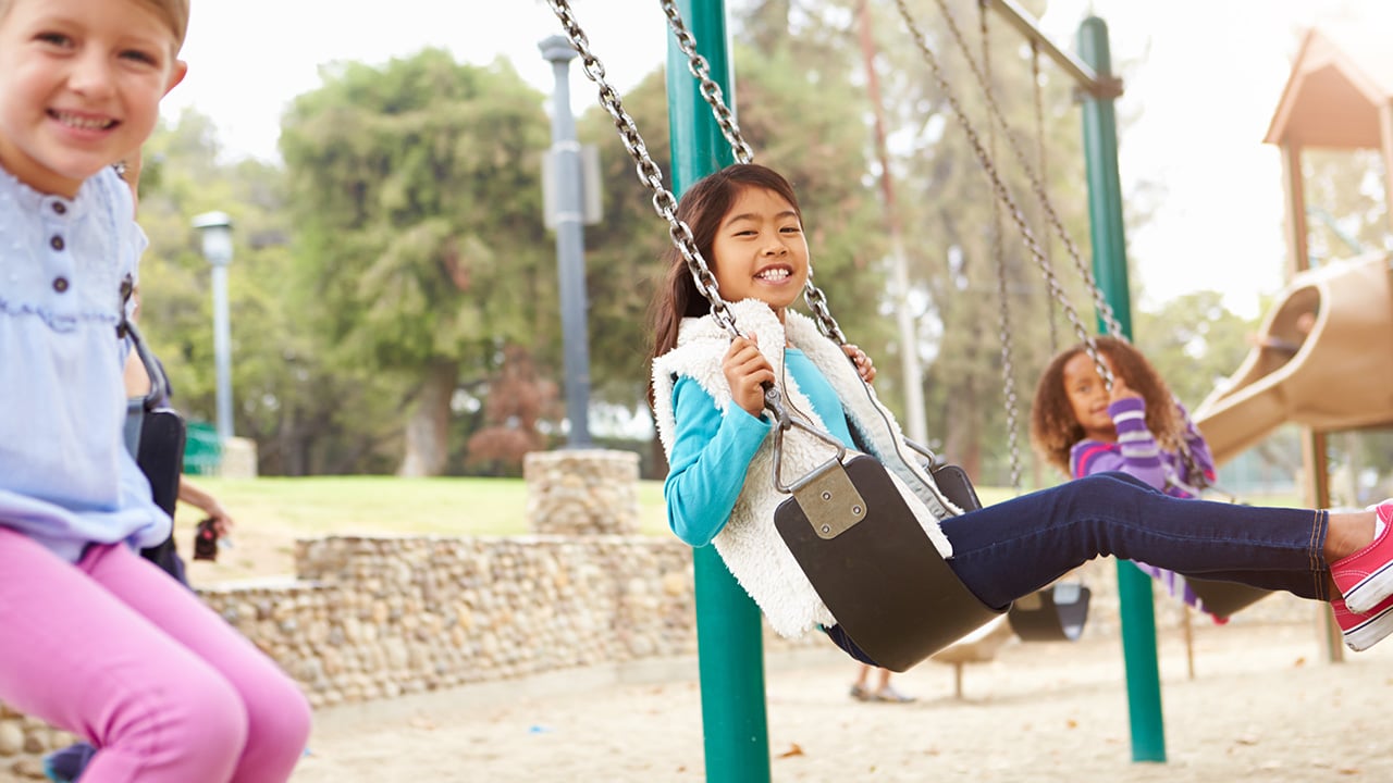 Three young girls swing on a playground