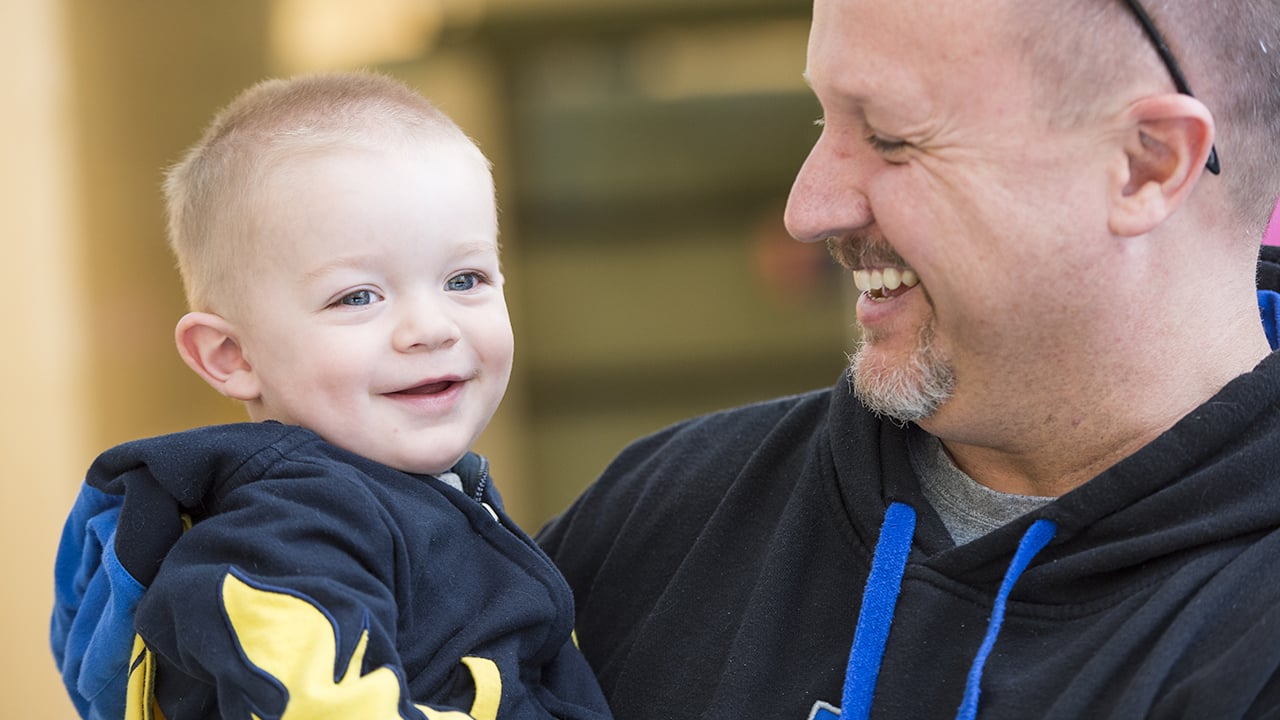 A smiling dad holds his toddler boy