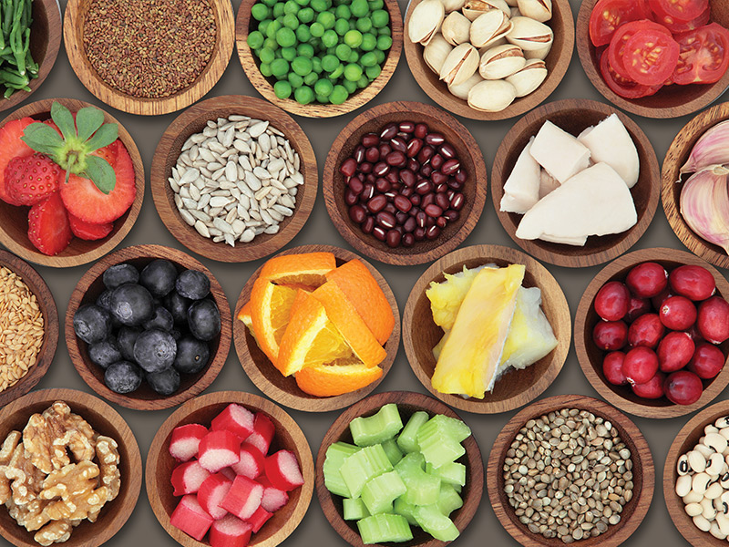 Various healthy foods such as oranges, blueberries, celery, and black beans in brown wooden bowls.