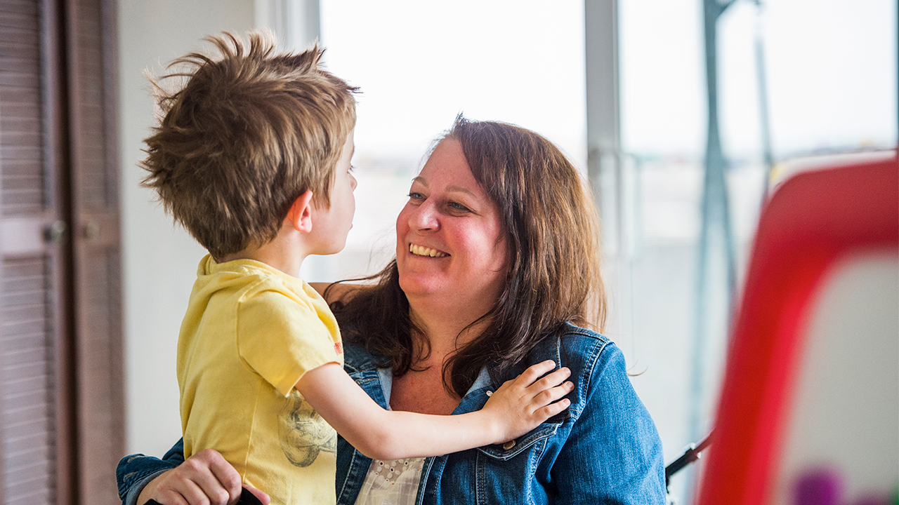 A smiling mom squats down to listen to her young son.