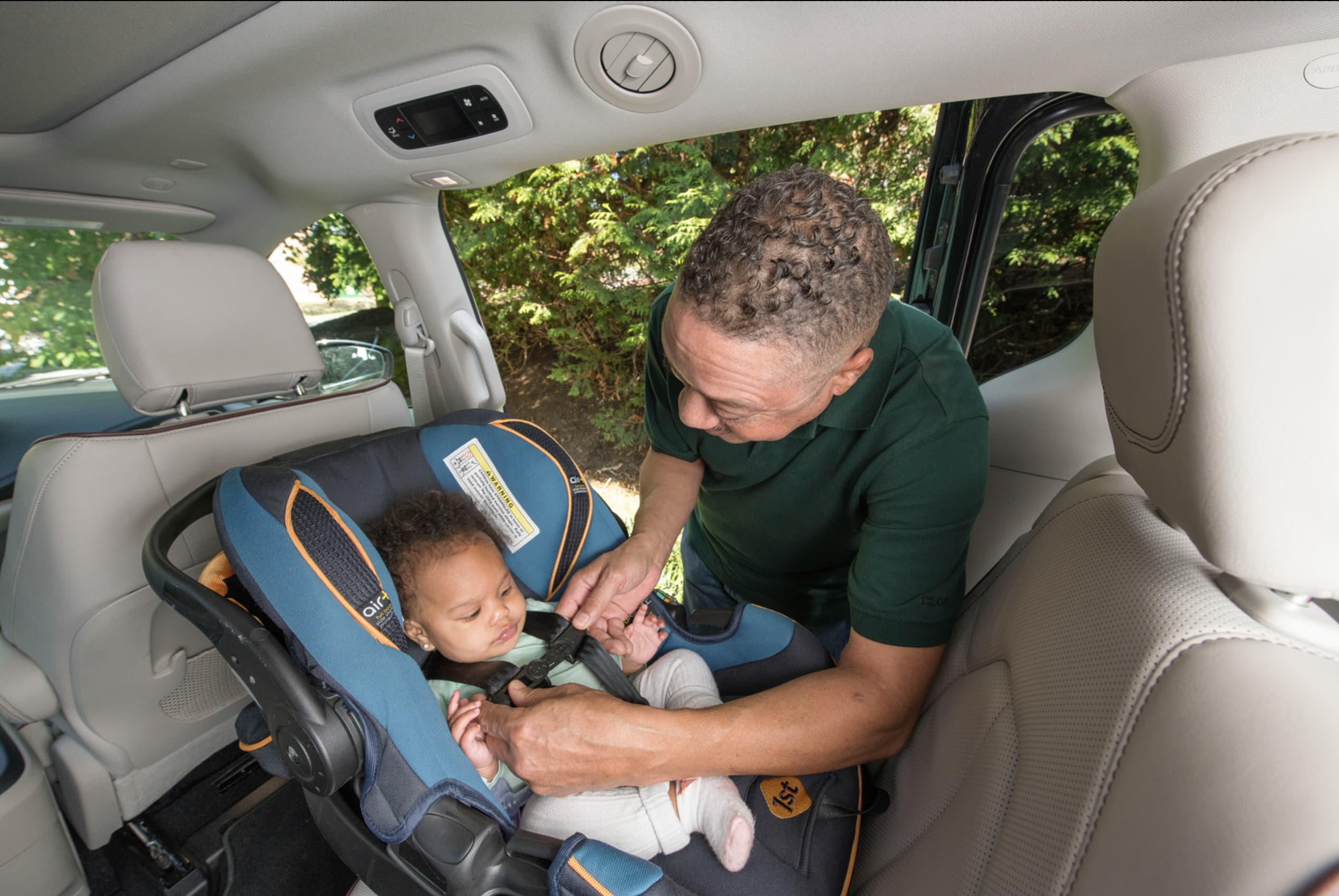 A man buckles the belt on a rear-facing car seat with a baby in it.