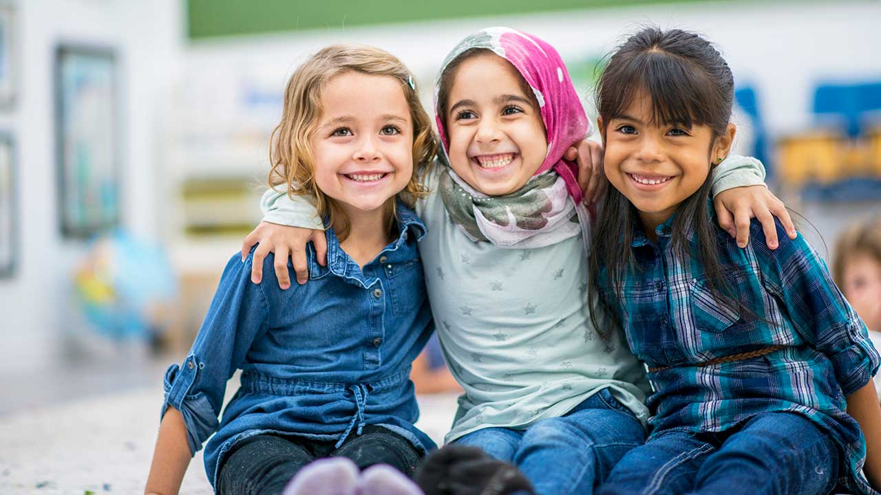 Three school age girls smile and hug each other.