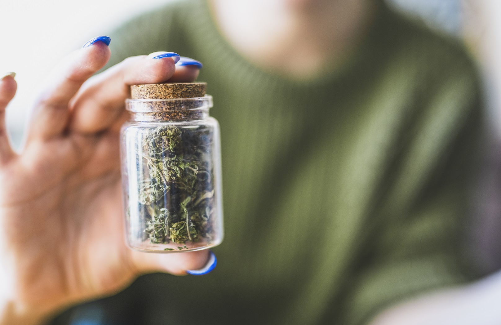 Closeup of a woman's hand holding a jar of marijuana.