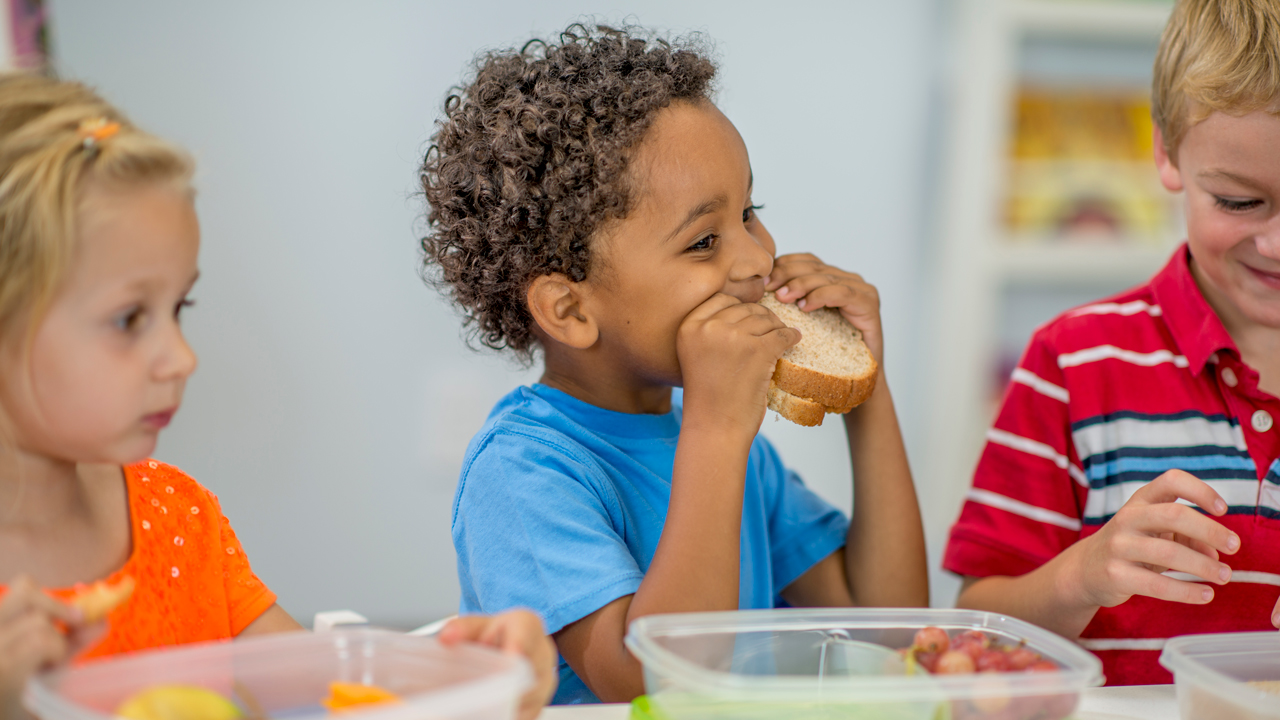 A child eats a peanut butter sandwich at a school lunch table.