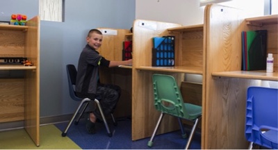 A boy sits in a chair at a desk partition.