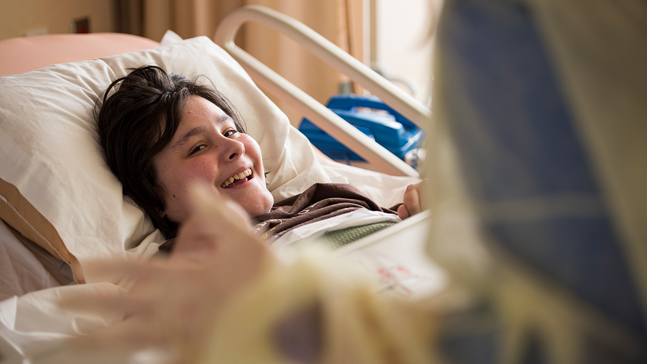 A kid lies in a hospital bed smiling.