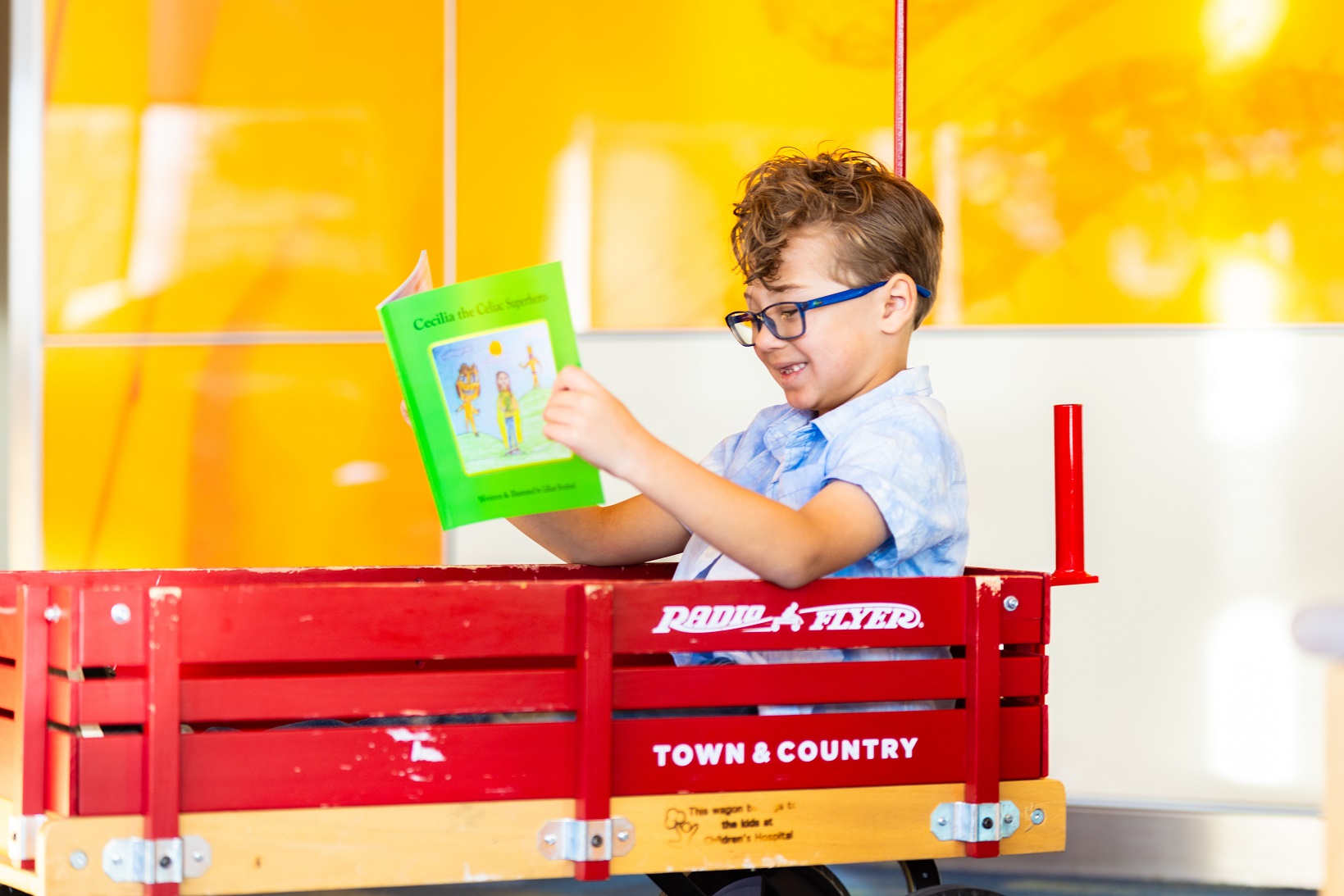 A boy with glasses reads a book in a Children's Hospital Colorado wagon.