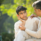 An adolescent boy and his father sit outside together while having a conversation.