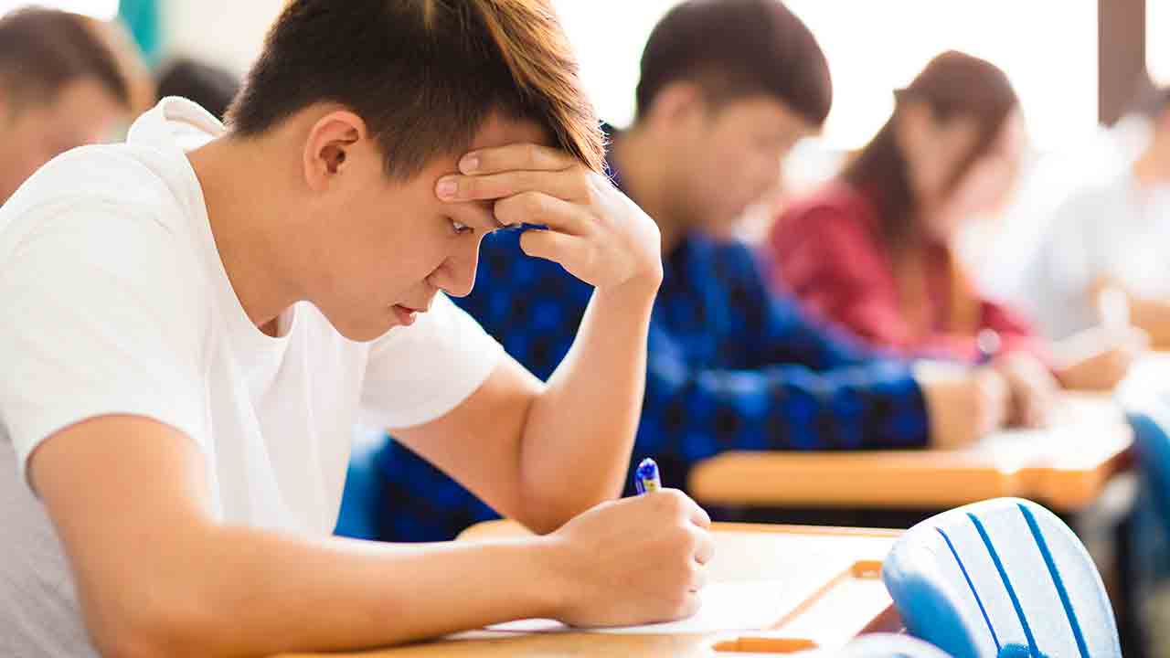 A teenage boy holds his head while studying at school.