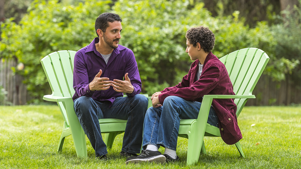 A father is having a conversation with his son outdoors sitting in lawn chairs.