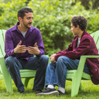 A father is having a conversation with his son outdoors sitting in lawn chairs.