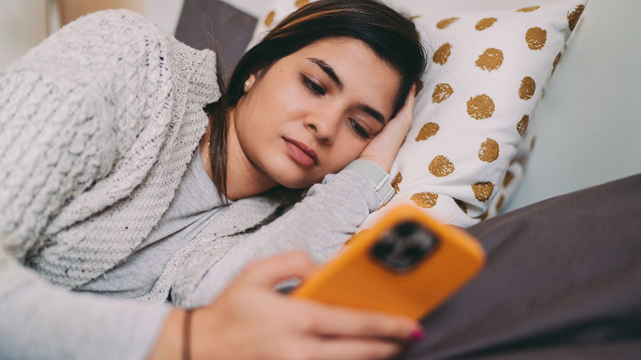 A teenage girl lies in bed while looking at her phone