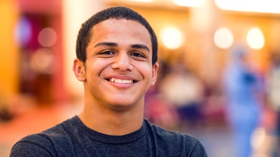 A boy with short dark hair and wearing a dark gray t-shirt smiles.