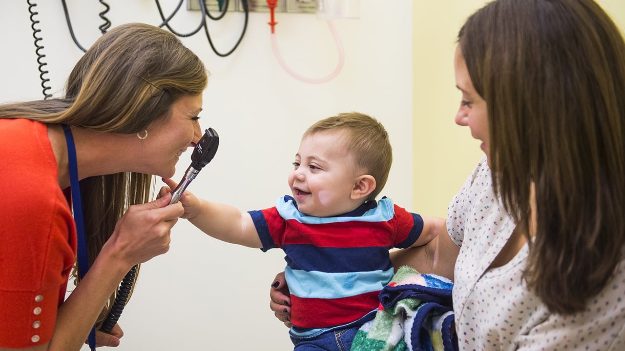 A healthcare provider examines a smiling baby during a well-child visit at the pediatrician.