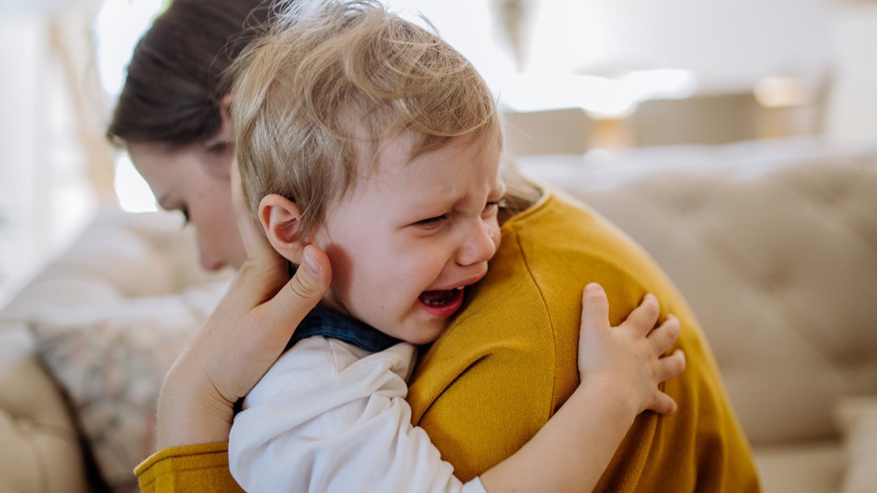 A toddler cries on his mother's shoulder as she tries to comfort him.